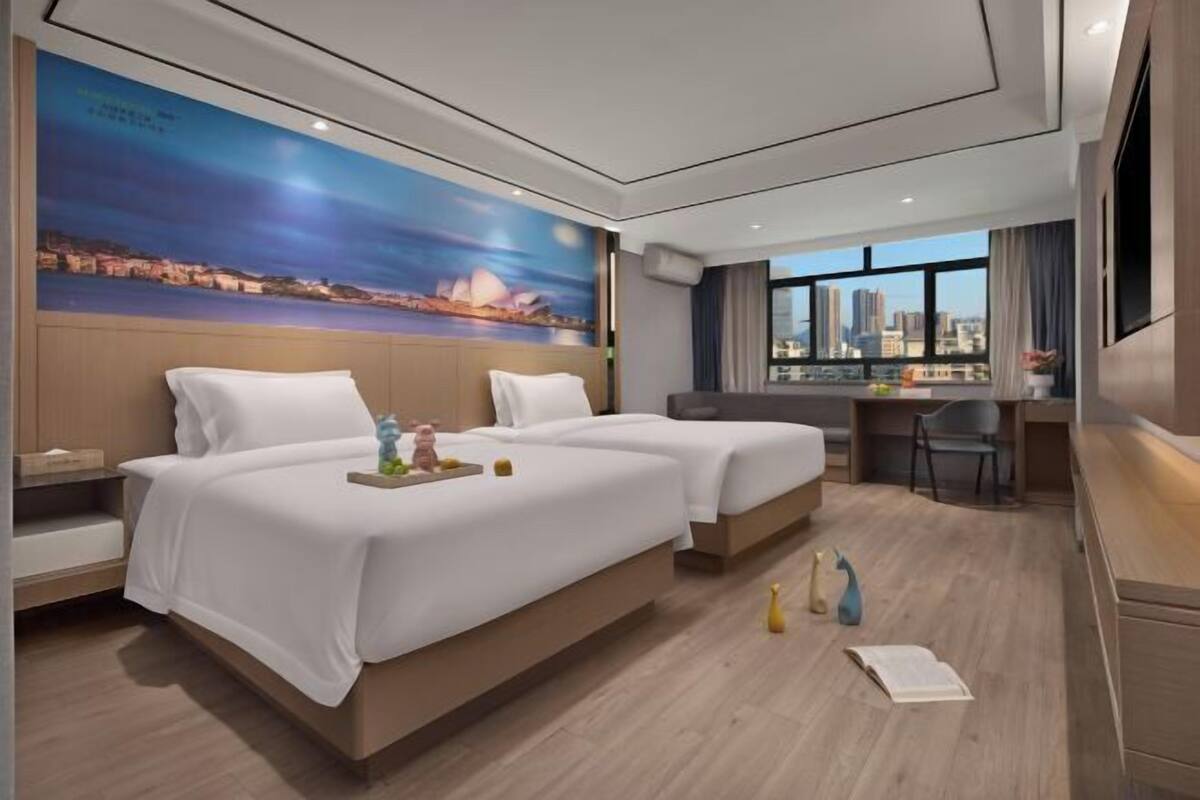 Habitación de hotel con dos camas, un escritorio, una silla y un ventanal con vista a la ciudad.