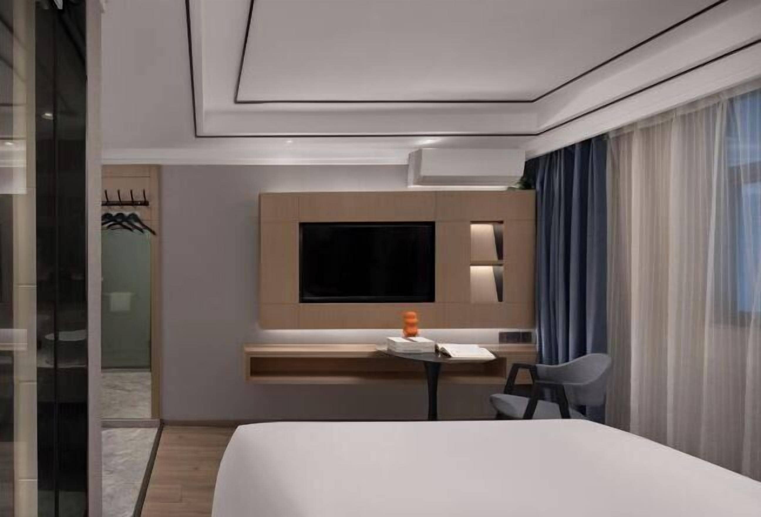A modern hotel room with a large bed, a desk with a chair, a flat-screen TV, and a window with sheer curtains.