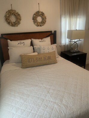 A neatly made bed with a quilted cover, two decorative wall hangings, and a bedside lamp on a nightstand. - Entire Unit (Conway)