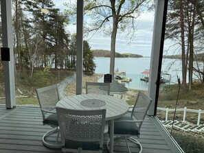 Un espacio al aire libre techado con una mesa y sillas, con vista a un lago con muelles y barcos.