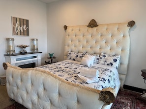 A bedroom with a tufted headboard, a patterned bedspread, and decorative pillows.