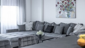 A modern living room with a grey sofa, a coffee table with a plant, and a painting of flowers on the wall. - Exclusive (top floor) new-build vacation apartment with distant views (Konstanz)