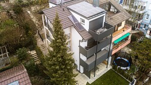 A modern multi-story building with solar panels on the roof, a balcony with outdoor seating, and a small trampoline in the yard. - Exclusive (top floor) new-build vacation apartment with distant views (Konstanz)