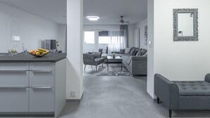 A modern living room with a grey sofa, a coffee table, and a TV. There is a kitchen area with a fruit bowl and a refrigerator. - Exclusive (top floor) new-build vacation apartment with distant views (Konstanz)