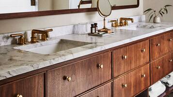 A bathroom with a marble countertop, gold faucets, and wooden cabinets.