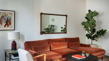Un soggiorno con un divano marrone, un tavolino, una poltrona, una lampada, uno specchio e una pianta grande.