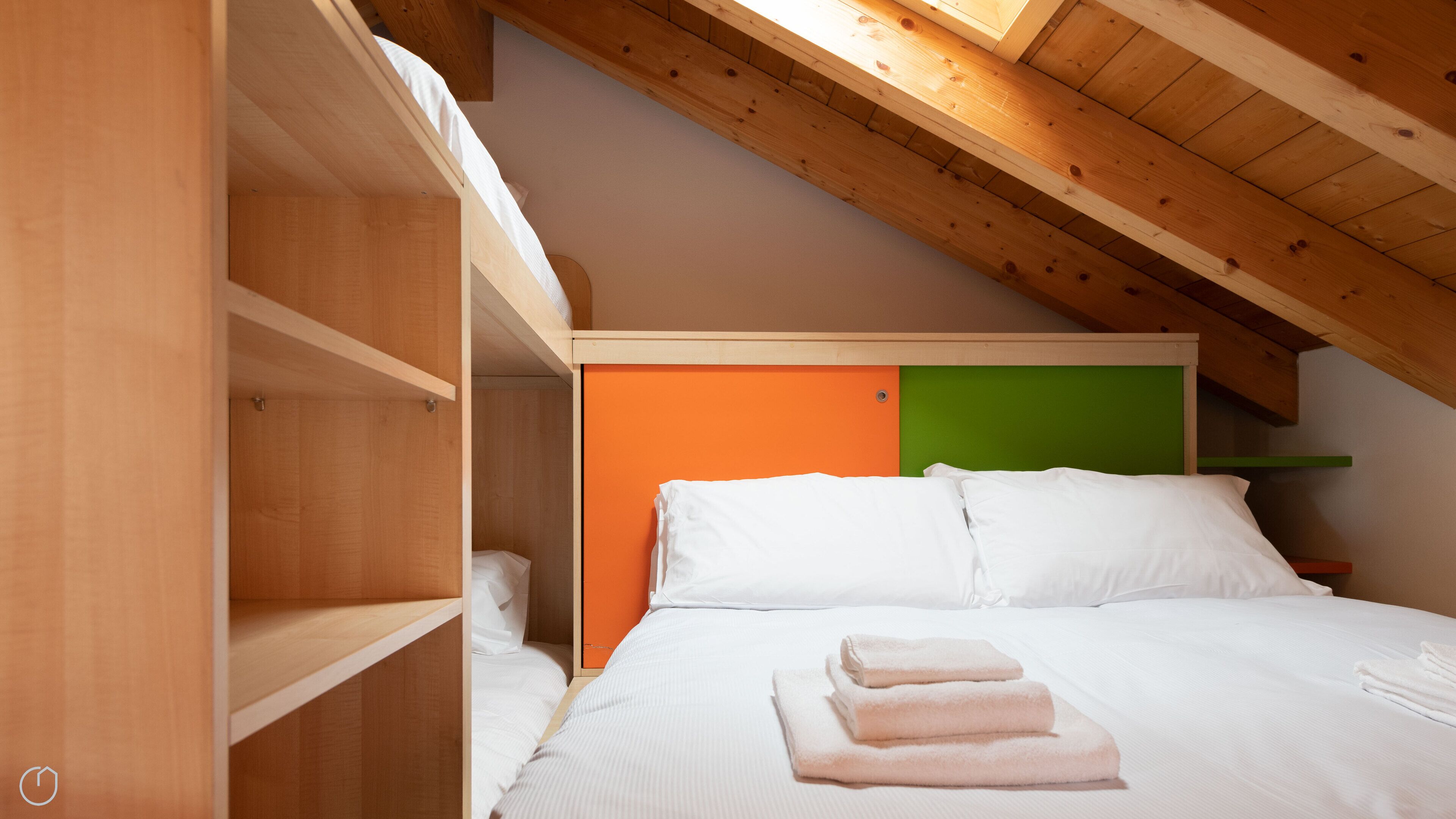 Un dormitorio con una cama litera, una pared verde y naranja, y un tragaluz.