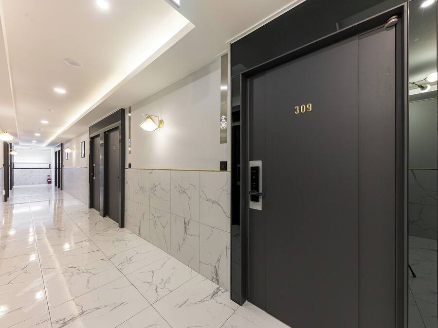 A modern hallway with marble flooring, a black elevator with the number 309, and wall-mounted lighting.