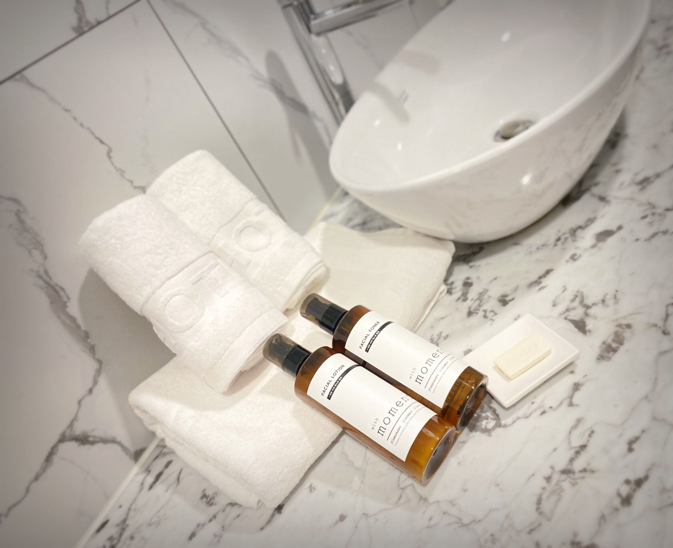 A bathroom with a white sink, a towel, and two bottles of facial lotion.