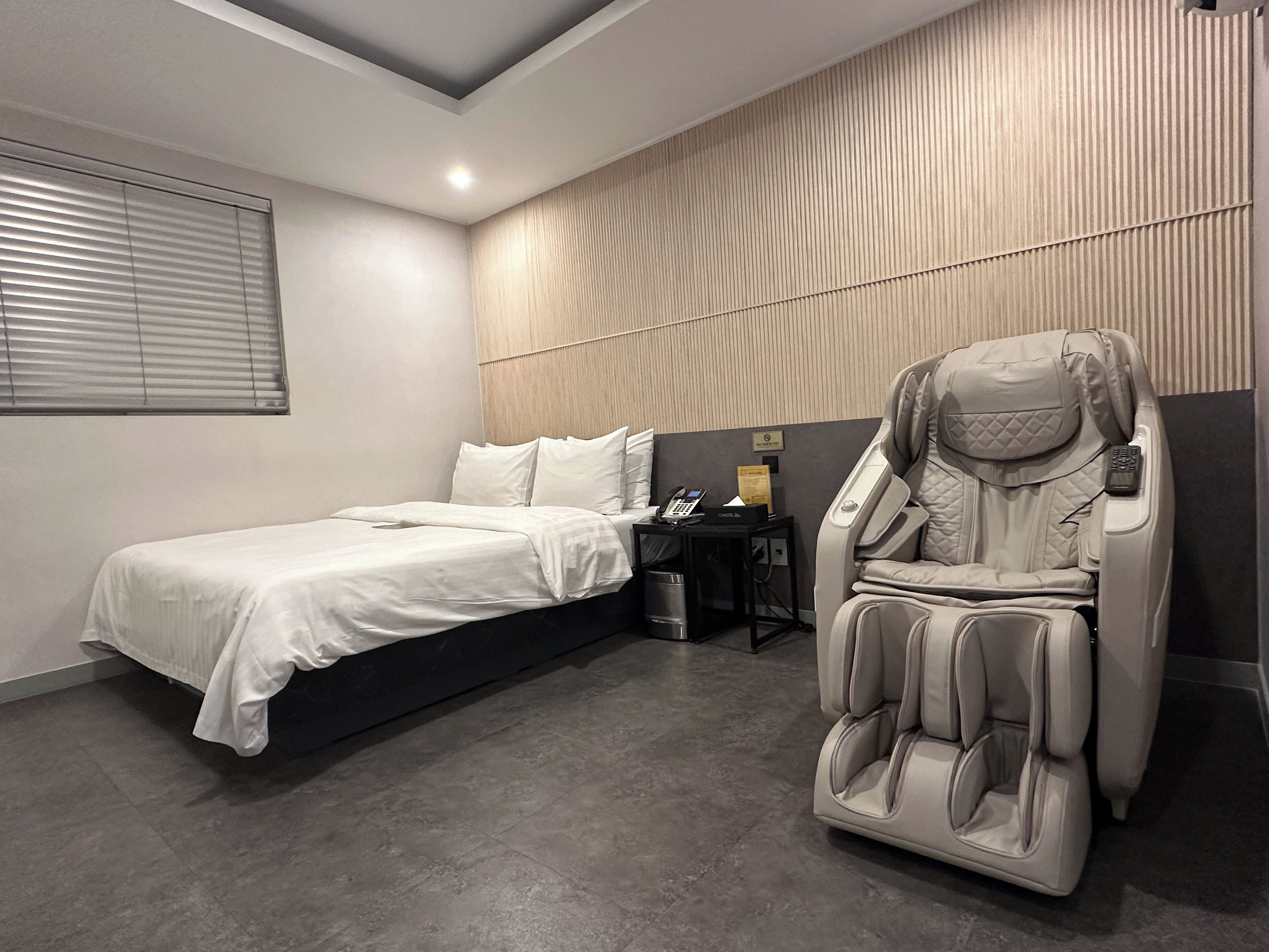 Ein modernes Hotelzimmer mit einem Bett, einem Massagesessel und einem kleinen Tisch mit Telefon und Taschentüchern.
