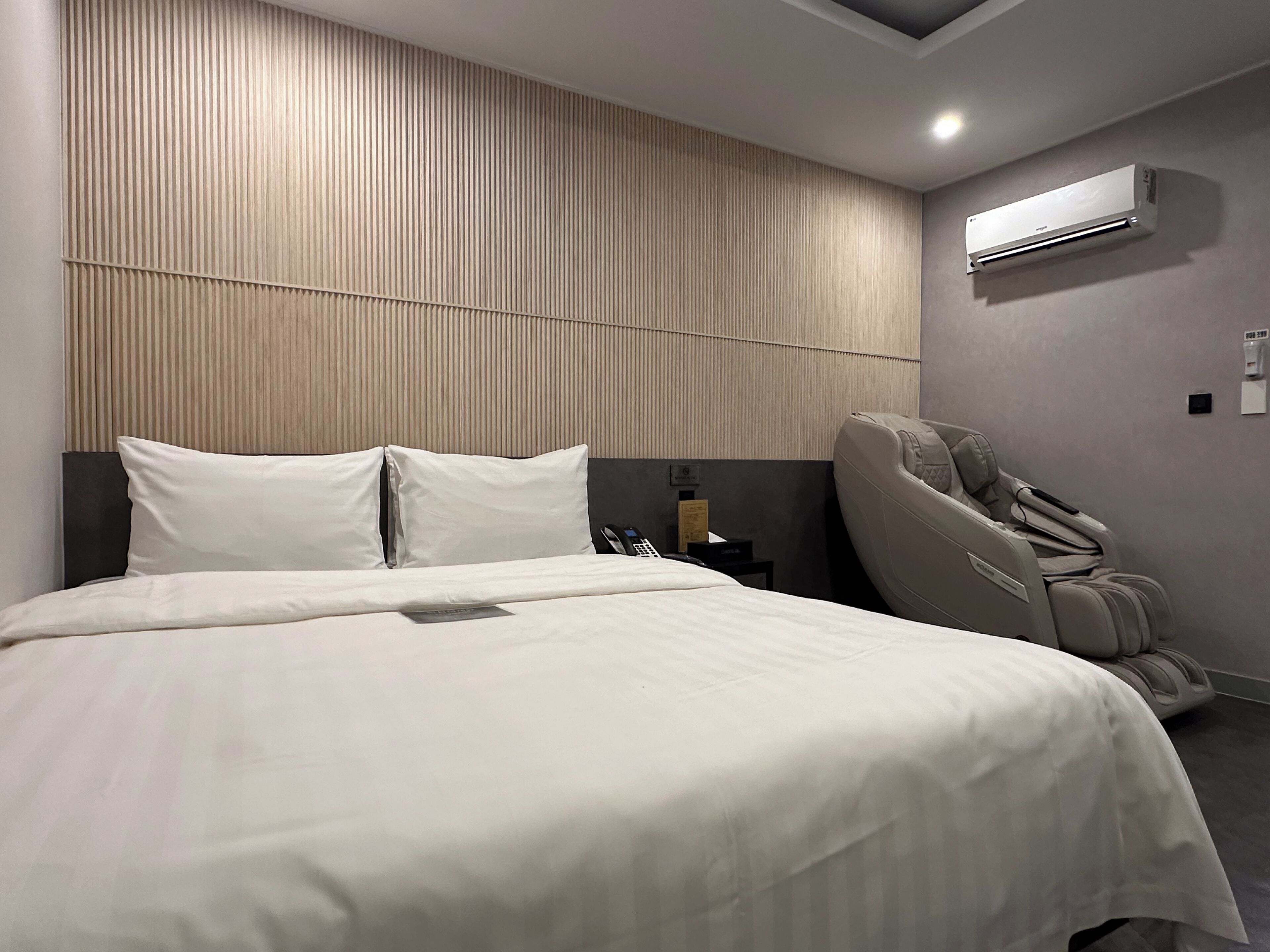 A modern hotel room with a large bed, a massage chair, and an air conditioning unit on the wall.