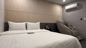 A modern hotel room with a large bed, a massage chair, and an air conditioning unit on the wall.