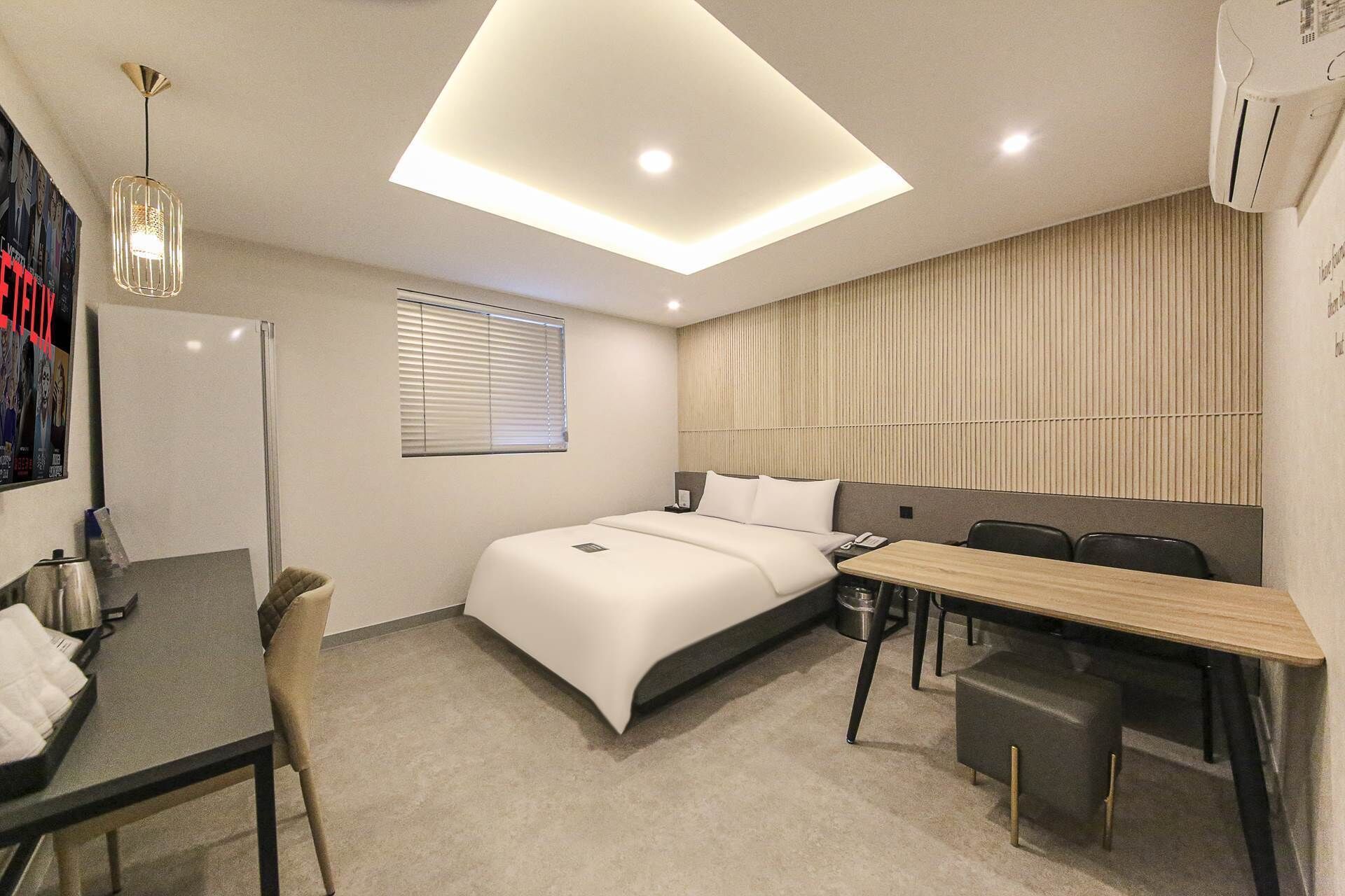 Een moderne hotelkamer met een bed, bureau, stoel en een plafondlamp.