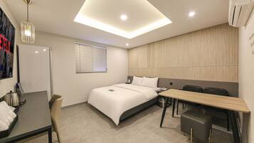 Een moderne hotelkamer met een bed, bureau, stoel en een plafondlamp.