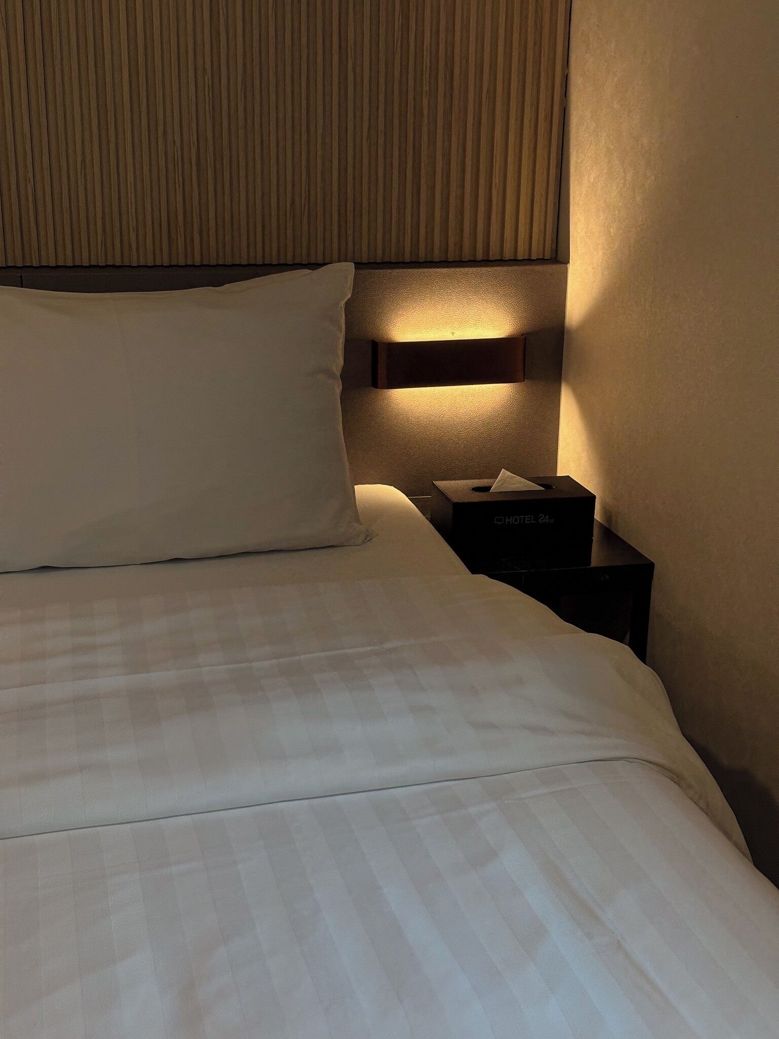 Una cama bien hecha con una almohada y una mesita de noche con una caja de pañuelos.