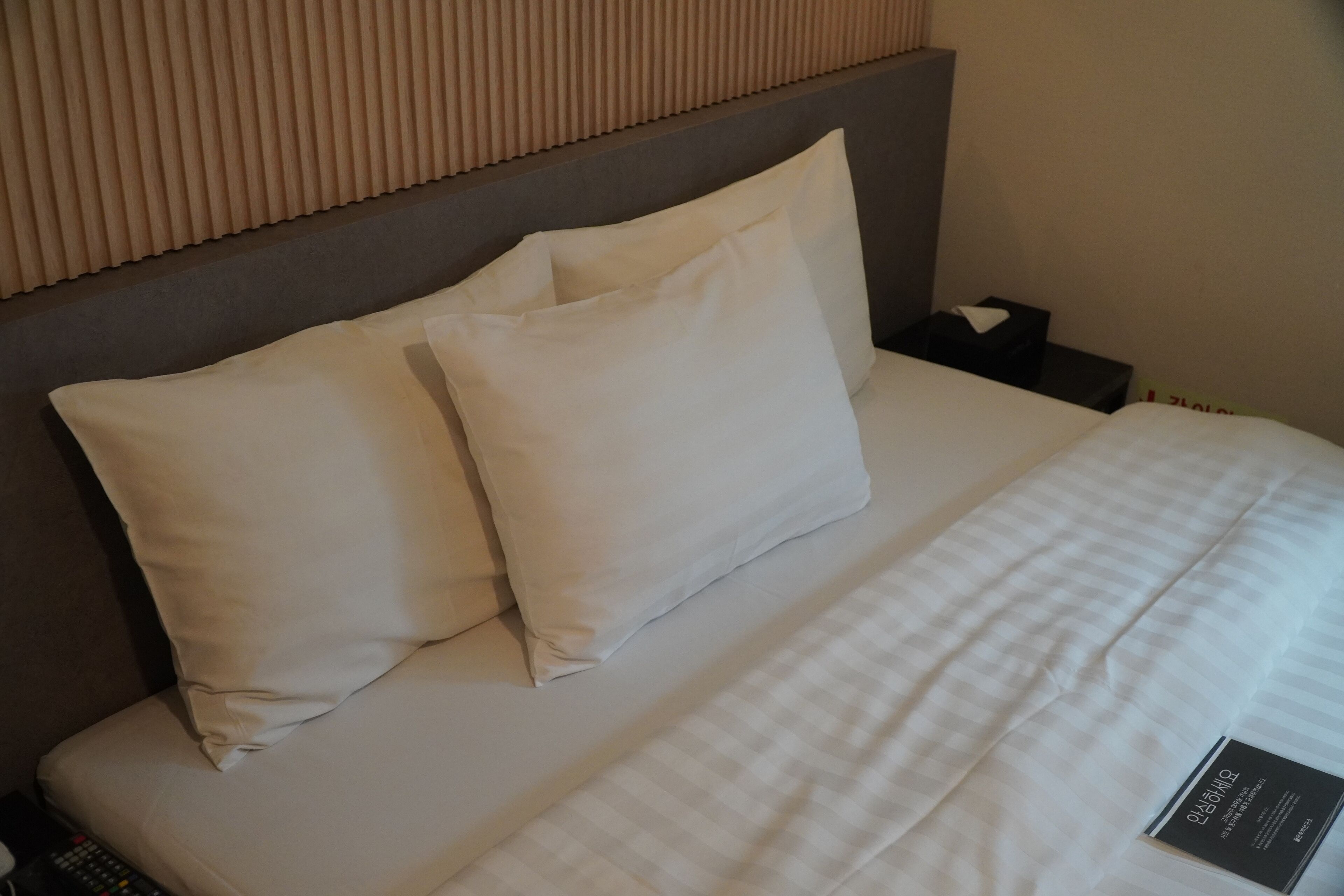 A neatly made bed with white linens and pillows, a remote control on the left, and a small black object on the right.