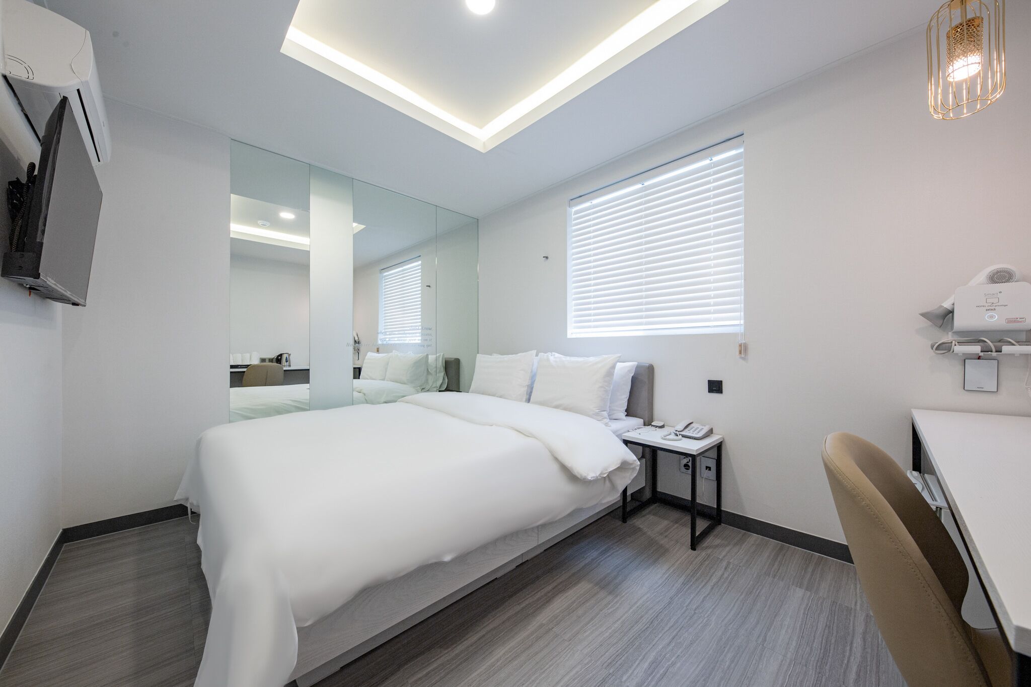 Een moderne hotelkamer met een groot bed, een bureau, een stoel, een spiegel en een plafondlamp.