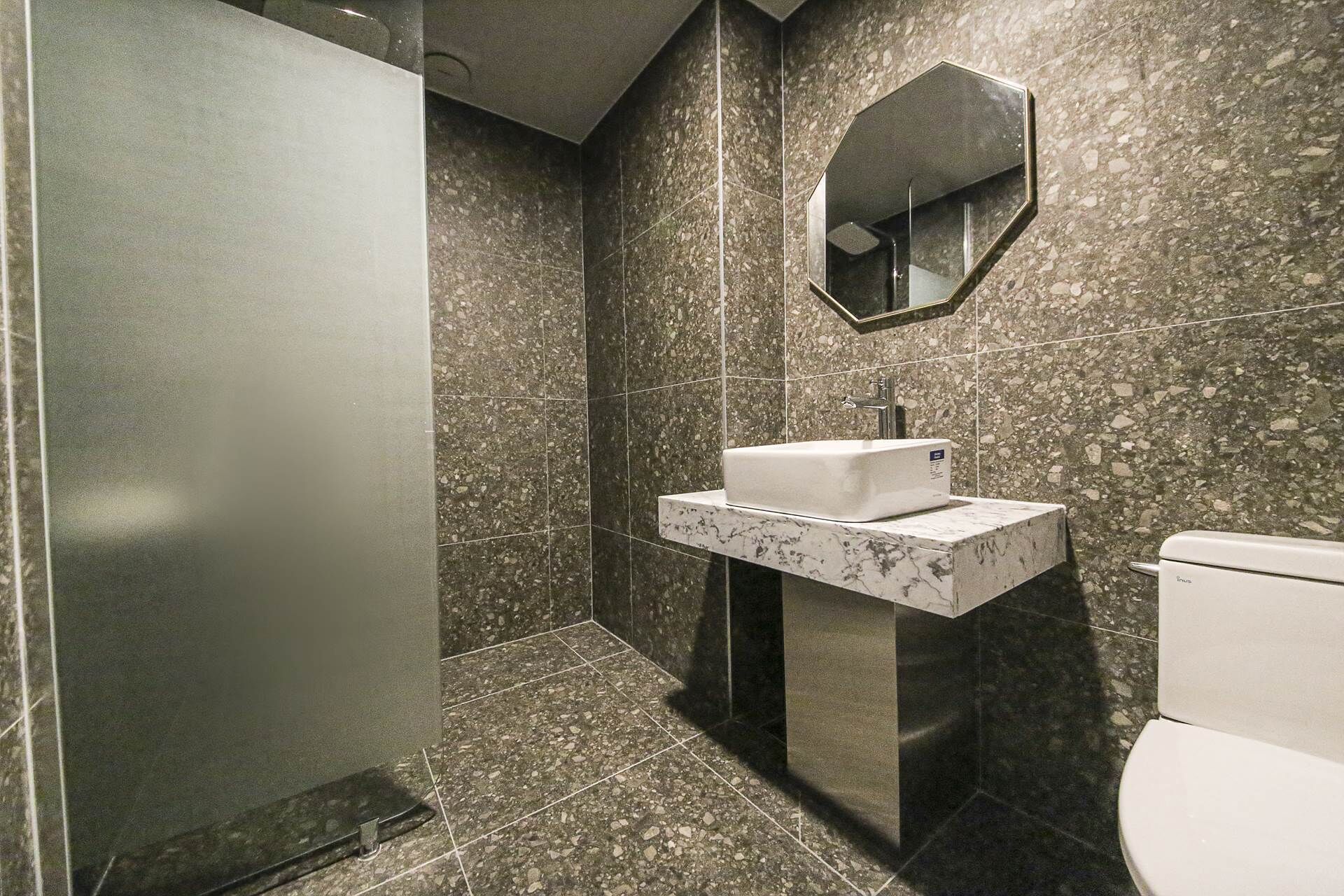 Un baño moderno con lavamanos de mármol, un espejo y un inodoro.