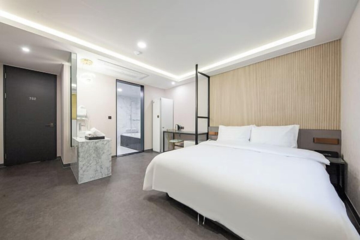 Habitación de hotel moderna con una cama grande, un escritorio con silla, un minibar y vistas a la ciudad desde la ventana.