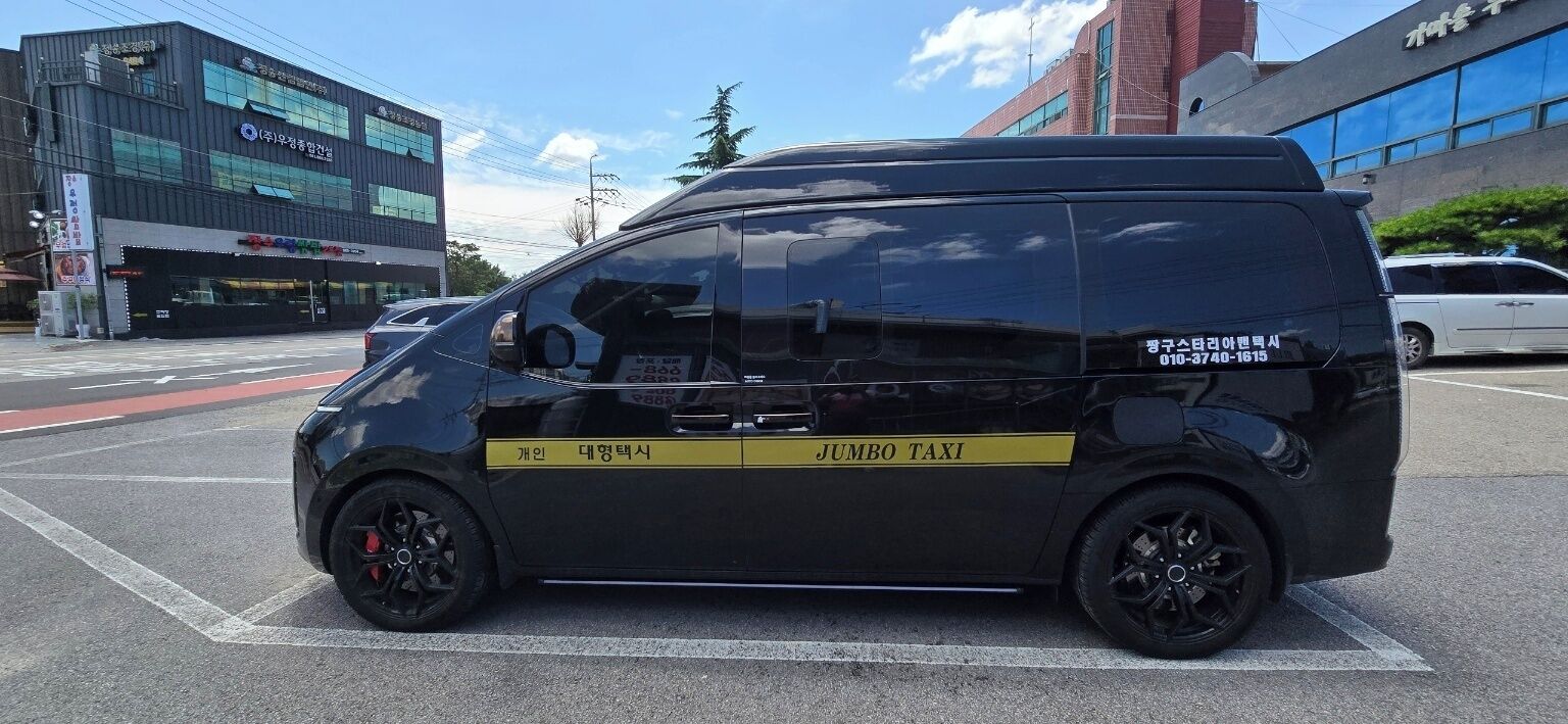 Una furgoneta negra con la leyenda "Jumbo Taxi" escrita en la carrocería estacionada en una calle.