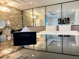 Quarto de hotel moderno com uma cama grande, divisória de vidro, televisão de tela plana e parede de tijolos.