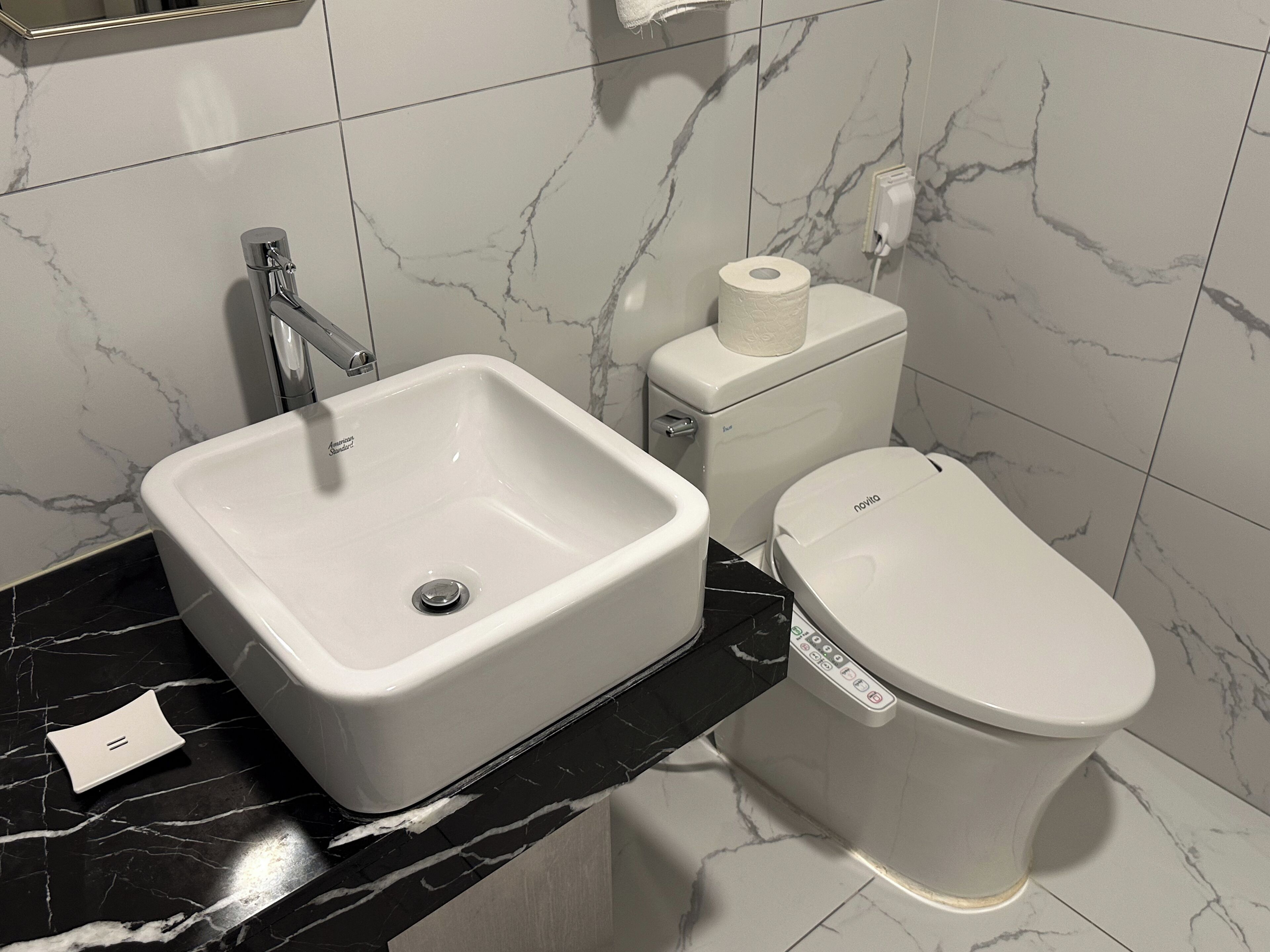 Ein Badezimmer mit einem weißen Waschbecken, einer Toilette und einer Wand mit Marmorplatten.