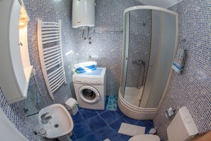 A compact bathroom with a washing machine, a glass shower enclosure, and a sink.