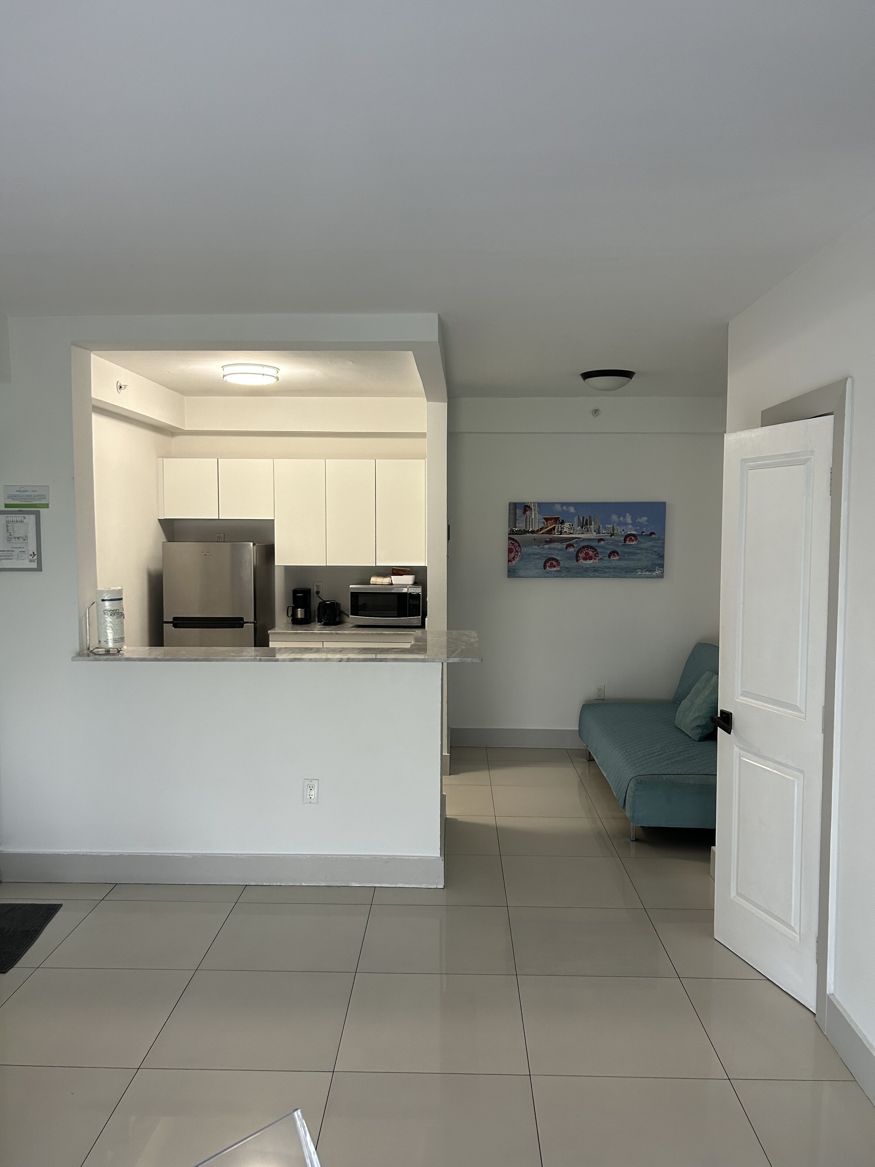 A modern kitchen with white cabinets, stainless steel appliances, and a tiled floor.