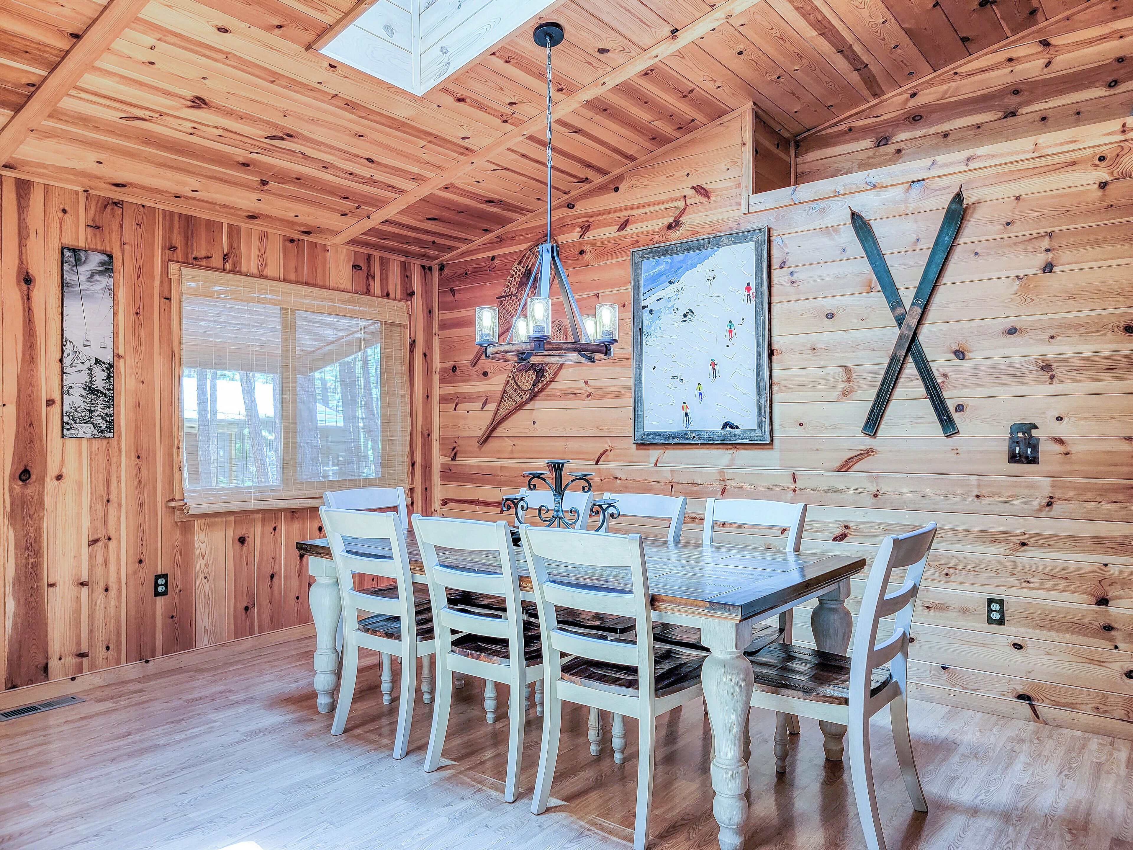 A wooden interior with a dining table and chairs, a chandelier, and a ski-themed wall art.