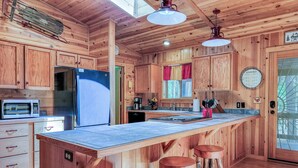 A wooden cabin kitchen with a large island, bar stools, a refrigerator, a microwave, and a coffee maker. - White Oak Retreat in Pinetop Country Club w/Firepit/Grill/Horseshoes! (Pinetop)