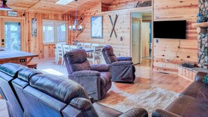 A cabin interior with wooden walls, a dining area, two leather sofas, a ceiling fan, and a mounted TV. - White Oak Retreat in Pinetop Country Club w/Firepit/Grill/Horseshoes! (Pinetop)