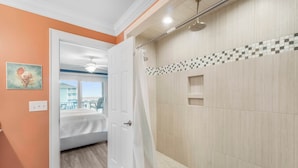 A bathroom with a shower, a door leading to a bedroom, and a view of a balcony.