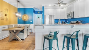 A modern kitchen with white cabinets, a stainless steel refrigerator, and a bar area with teal stools.