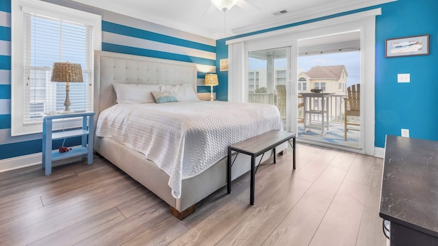 A bedroom with a bed, a nightstand, a lamp, a ceiling fan, and a view of the outside.