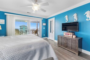 A bedroom with a large bed, a ceiling fan, a TV, and a view of the ocean.