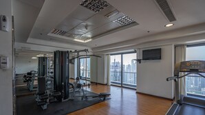Uma academia ampla com diversos equipamentos de exercício, janelas grandes com vista para a cidade e esteira.
