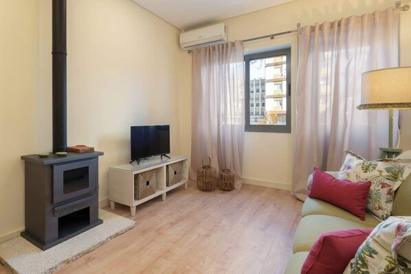 A living room with a fireplace, a television, a sofa, and a window with curtains. - Gaya Avenue 102 - Flat w/ Balcony (Vila Nova de Gaia)