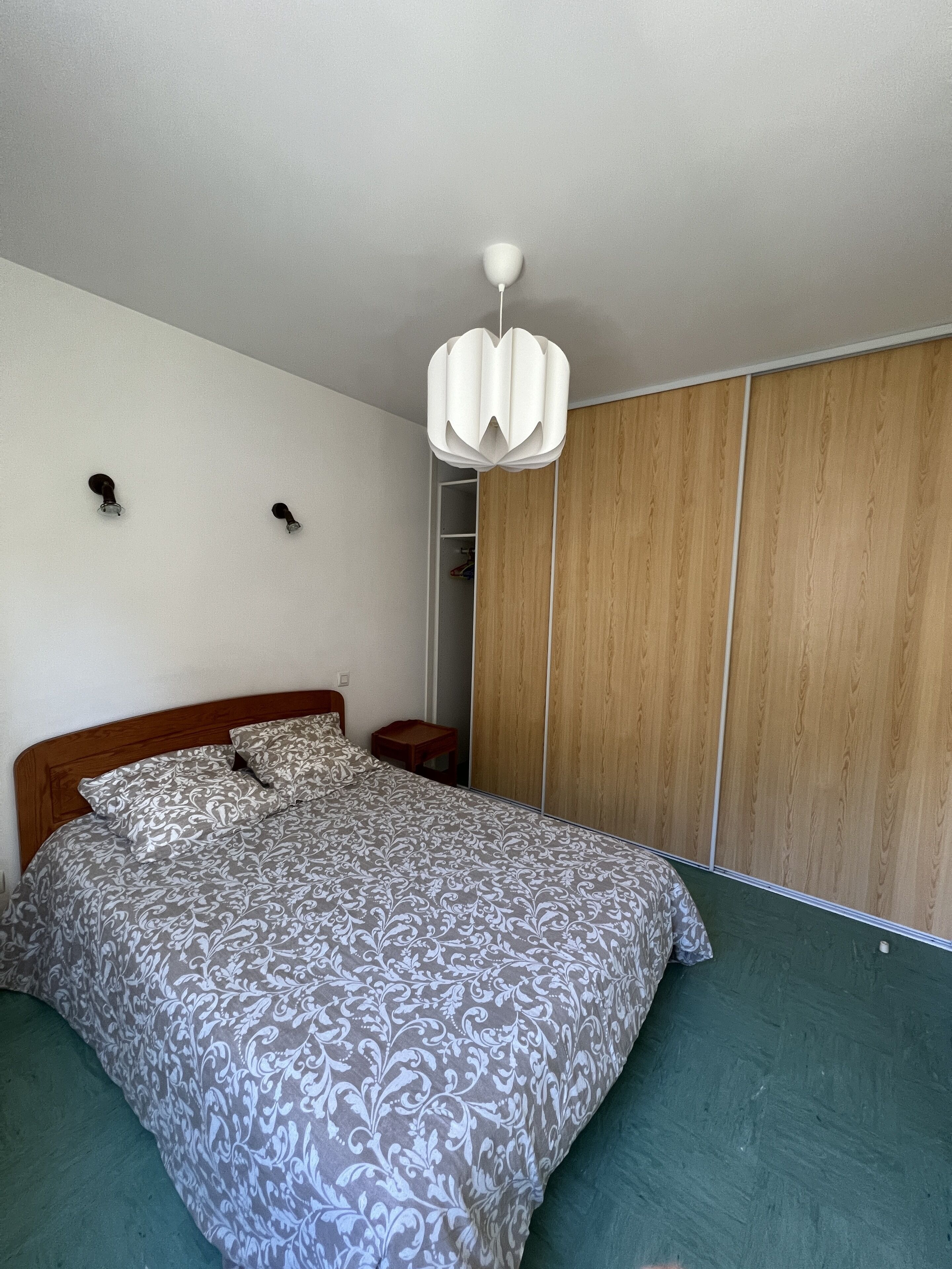 Une chambre à coucher comprenant un lit, une armoire en bois, une table de chevet et un luminaire suspendu.