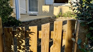 Une clôture en bois devant une maison avec un toit en tuiles et une porte à volets.