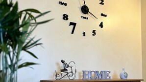 Une pièce avec une horloge murale, une commode en bois avec des tiroirs, une plante en pot et un objet décoratif posé sur la commode.