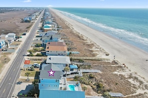 Stunning beachfront homes line the coast, offering access to the sandy beach via a paved walkway.