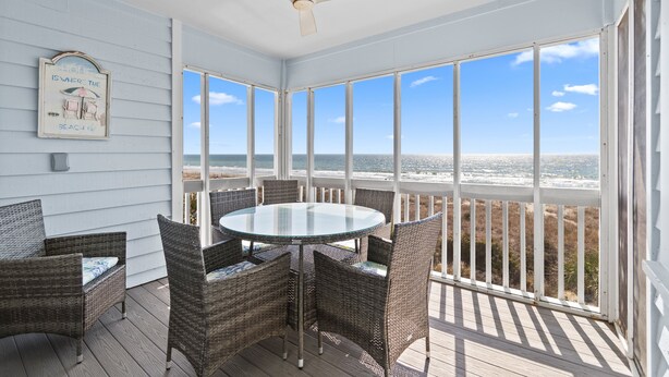 Un espacio al aire libre techado con muebles de mimbre, una mesa de vidrio y vista a la playa.