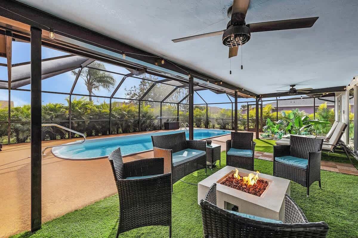 A covered outdoor area with a pool, wicker furniture, and a fire pit.