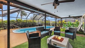 A covered outdoor area with a pool, wicker furniture, and a fire pit.