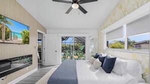 A bedroom with a bed, a ceiling fan, a TV, and a view of the outdoors.