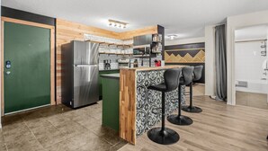 A compact kitchen with a refrigerator, microwave, and sink. There are three bar stools and a small island with a patterned backsplash. - 9 Peaks | Scandinavian | Pool | Hot Tub | Beach (Invermere)