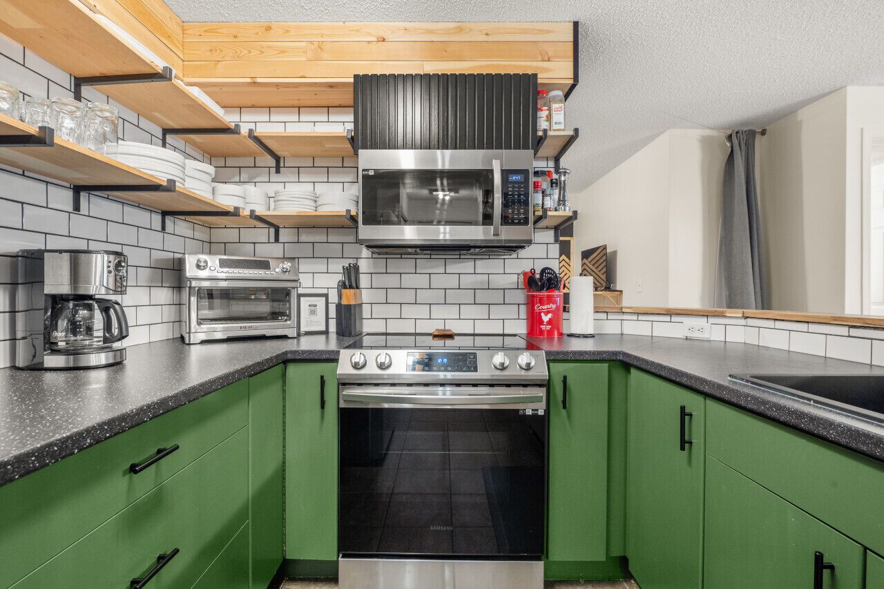 A kitchen with green cabinets, a stainless steel oven, a microwave, and a coffee maker.
