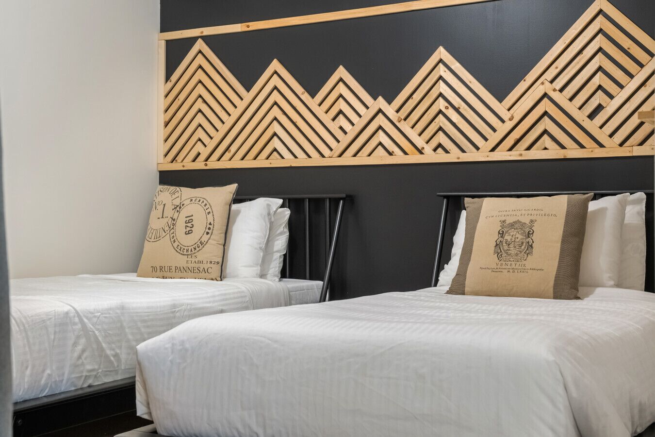 Une chambre d’hôtel avec deux lits simples, chacun agrémenté d’un oreiller au motif rétro.