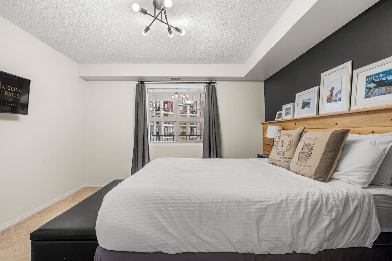 Un dormitorio con una cama grande, cabecera de madera, lámpara en el techo, vista de un edificio a través de la ventana y un cartel en la pared.