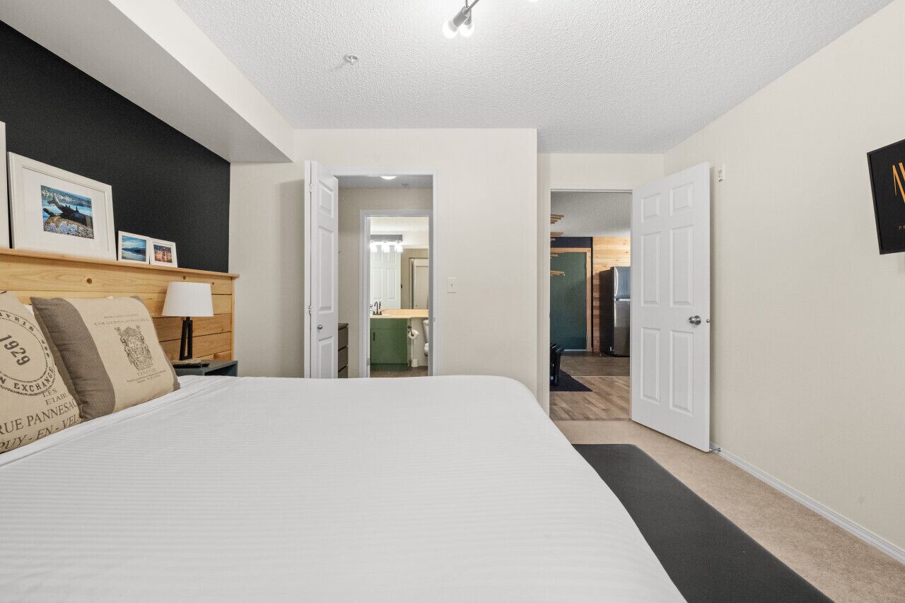 Hotellihuone, jossa on suuri sänky, yöpöytä lampun kanssa, puinen pääty ja sängyn yläpuolella oleva kehystetty kuva.